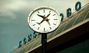 Zegar z samolotem na tle lotniska. Odprawa online co dalej na lotnisku? Czas leci!