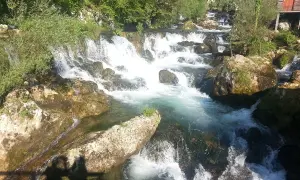 Vattenfall och klippor vid en flod nära Banja Luka. En liten röd stuga skymtar bland träden.