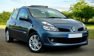 Un Renault Clio azul aparcado en un camino rural. El coche tiene un techo solar y llantas plateadas.