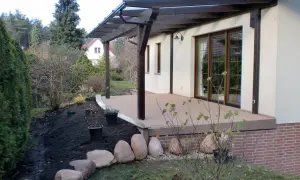 Terrasse sanieren: Neue Holzterrasse mit Überdachung, daneben frisch aufgeschüttete Erde und Steine für die Gartengestaltung.