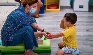 Niña recibe terapia ocupacional infantil, con un terapeuta aplicando pintura roja en su brazo.