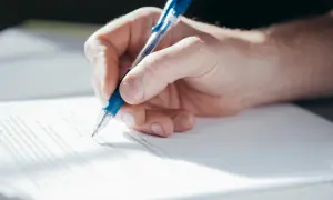 Dłoń pisze długopisem na dokumencie, który może być pełnomocnictwem do zarządzania nieruchomością.
