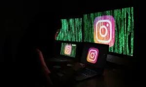 Osoba pracuje przy komputerze, na ekranach widnieje logo Instagrama i zielony kod. Szuka informacji, jak odzyskać zhakowane konto na Instagramie.