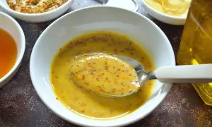 Cuchara con salsa miel y mostaza, lista para aderezar. Ingredientes en cuencos alrededor.