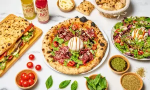 Une pizza diavola appétissante, garnie de charcuterie, burrata et roquette, accompagnée d'un sandwich, de salade et de boissons bio.