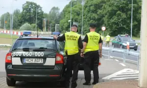 Funkcjonariusze Służby Celno-Skarbowej w kamizelkach odblaskowych przy radiowozie. Zarobki w tej służbie są adekwatne do odpowiedzialności.