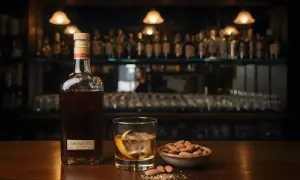 Butelka amaretto o głębokim, bursztynowym kolorze, szklanka z lodem i skórką pomarańczy, miseczka migdałów.