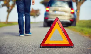 Triángulo de emergencia en carretera. Persona se aleja de coche averiado, lista para proteger, alertar y socorrer.