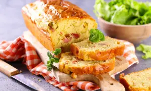 Un cake chorizo poivron, doré et moelleux, coupé en tranches sur une planche en bois. Une salade verte est servie à côté.