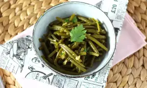 Un tazón de judías verdes salteadas con ajo y perejil, servido sobre un mantel de mimbre.