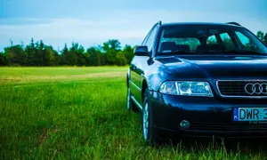 Ciemne Audi A4 B6 2.0 benzyna na tle zielonej łąki i błękitnego nieba.