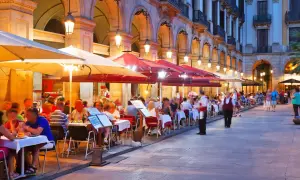 Kvällssol över många uteserveringar med folk som äter och dricker. En livlig atmosfär på restauranger i Barcelona.