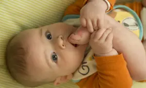 Urocze 5 miesięczne dziecko odkrywa swoje stópki, wkładając je do buzi.