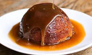 Un delizioso sticky toffee pudding, ricoperto da una cascata di salsa al caramello, servito su un piatto bianco.