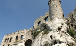 Zamek Ogrodzieniec jak wyglądał: ruiny kamiennego zamku na skale, z wieżą i murami, pod błękitnym niebem.