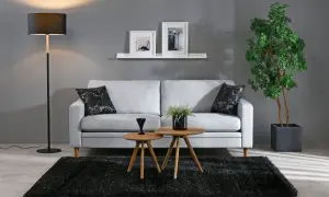 Grå soffa med svarta marmorkuddar, två runda träbord, svart matta och golvlampa i modern stil.