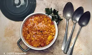 Herzhaftes Bohneneintopf Rezept mit Speck und Kartoffeln, garniert mit Petersilie. Daneben liegen drei Löffel bereit.