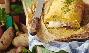 Herzhaft gefüllte polpette di patate, goldbraun paniert, mit geschmolzenem Käse im Inneren. Frische Kartoffeln liegen daneben.