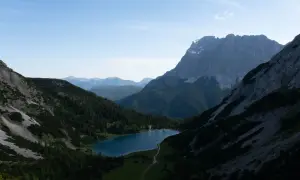 Ein Bergsee liegt eingebettet zwischen steilen Hängen, die wie ein vorderer Drachenkopf wirken. Nadelbäume bedecken die Flanken, im Hintergrund ragen weitere Gipfel auf.