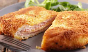 Cotoletta alla valdostana dorata e croccante, farcita con prosciutto e formaggio filante, servita su un piatto grigio con un contorno di insalata verde.