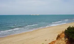 Playa de arena dorada con mar turquesa y una estructura en el horizonte. Un rincón idílico de las calas Chiclana.