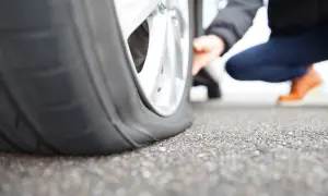 Pneu crevé que faire ? Une personne accroupie examine un pneu à plat sur la route.