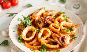 Délicieuse recette encornet à la sauce tomate, garnie de persil frais. Des tomates cerises et de l'ail sont disposés sur le côté.