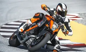 Motocyklista w kombinezonie pochyla się na torze wyścigowym na pomarańczowym motocyklu KTM Super Duke.