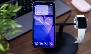 Nowy iPhone z najnowszym iOS, pokazujący widżety pogody i zegara. Obok stoi Apple Watch.
