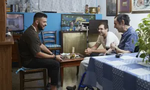Tre uomini discutono in un salotto. Uno di loro, seduto su una sedia a rotelle, potrebbe chiedere quanto prende di pensione un dializzato.