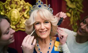 Camilla, drottningen, får smink och hår fixat. Hon bär en tiara och ett blått halsband.