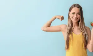 Donna sorridente mostra il bicipite e una ciotola di insalata, simbolo di una dieta per stitichezza menù settimanale salutare e benessere.