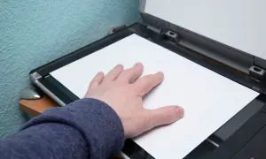 Dłoń dociska białą kartkę papieru do otwartego skanera.