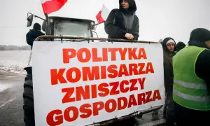 Rolnicy protestują z transparentem "Polityka komisarza zniszczy gospodarza" na tle traktora.