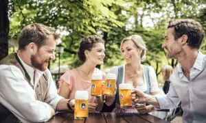 Coppie brindano con boccali di zwickl birra sotto alberi verdi.