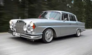 Silver Mercedes från 60-talet glider fram på en väg, omgiven av skog. Klassiska bilar som denna är tidlösa.