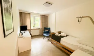 Pokój hotelowy z łóżkiem, biurkiem, fotelem i obrazem z lasem.
