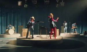 Lady Gaga w czerwonych rajstopach i niebieskiej sukience tańczy na scenie, podczas gdy zespół gra. Tekst "die with a smile" może być inspiracją do tej sceny.