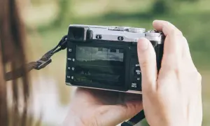 Dłonie trzymają aparat, który może być dobrym aparatem fotograficznym do 500 zł. Na ekranie widać krajobraz.