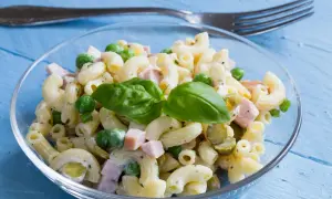 Ein cremiger Nudelsalat mit Erbsen, Schinken und Gurken, garniert mit Basilikum. Perfekt als schnelles rezept nudelsalat.