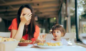 Zmęczona mama zakrywa twarz, gdy jej bananowe dzieci odmawiają jedzenia.