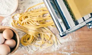 Frischer Tagliatelle-Nudelteig mit Eiern, Mehl und Nudelmaschine auf Holzbrett.