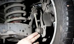 Dłoń mechanika wskazuje na zużyty stabilizator w zawieszeniu samochodu.