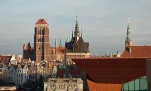 Widok na zabytkowe kamienice i wieże kościołów w śródmieściu Gdańska. W tle nowoczesna, miedziana bryła budynku.