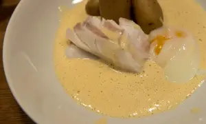 En portion torskrygg med pocherat ägg och potatis i en krämig sås. Perfekt för en middag med vin till torskrygg.