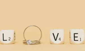 Un anillo inicial de oro con un diamante, junto a cubos que forman la palabra "LOVE".