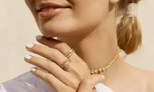Manos con manicura blanca luciendo dos anillos de **joyería Suárez anillos** y un collar dorado.
