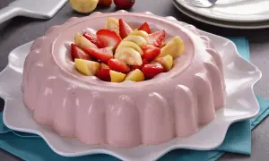 Deliciosa gelatina de fresa con trozos de fresa y guayaba fresca en el centro, servida en un plato blanco ondulado.