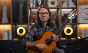Mężczyzna z gitarą uczy, jak nauczyć się nut. W tle półki z książkami i dekoracjami.