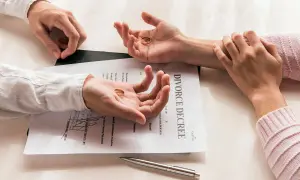 Dwie dłonie trzymają obrączki na tle dokumentu "DIVORCE DECREE". Czy do rozwodu potrzebny jest akt małżeństwa? Pytanie wisi w powietrzu.
